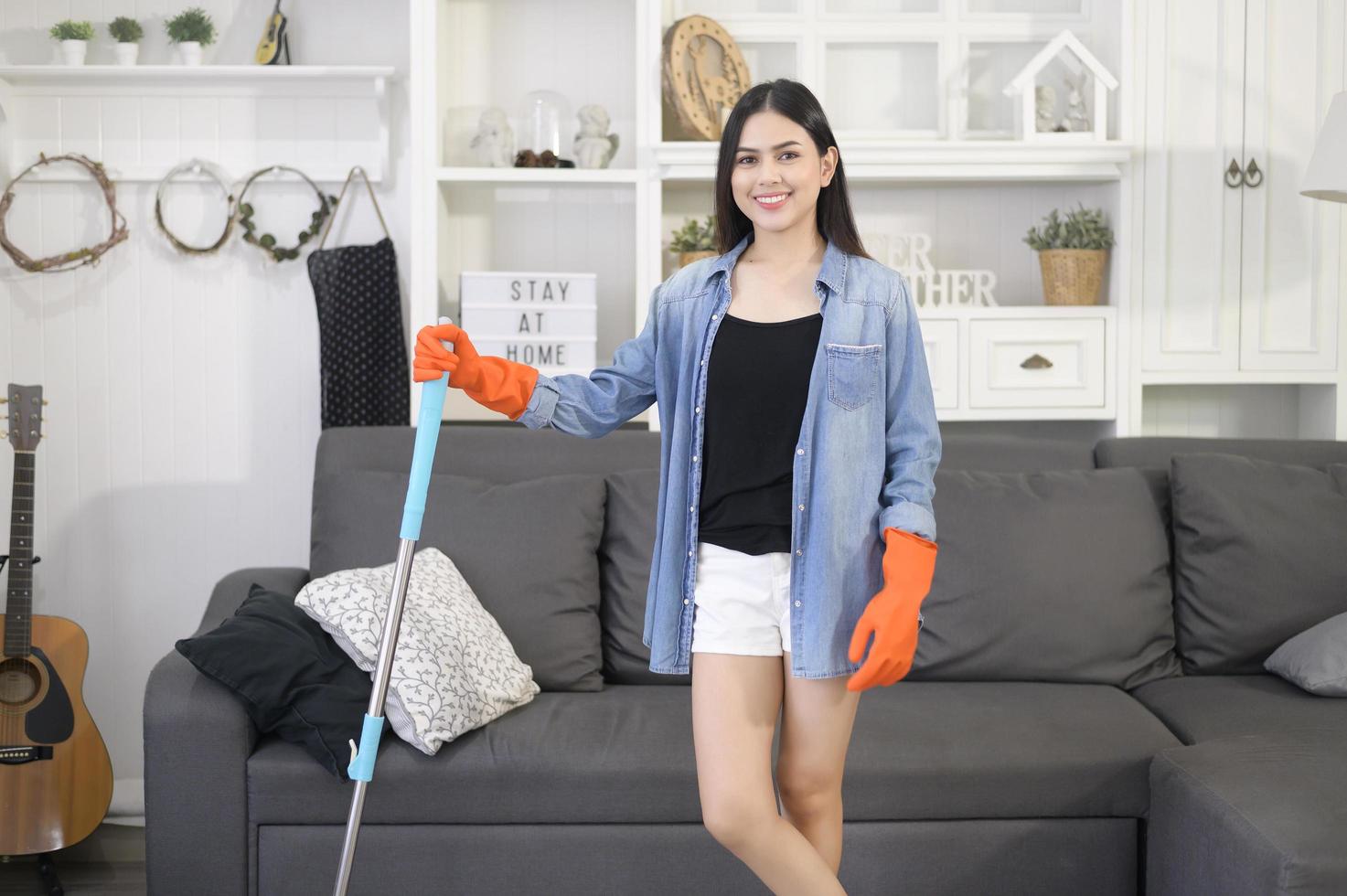 glückliche junge Frau, die den Boden mit Mopp im Wohnzimmer säubert foto