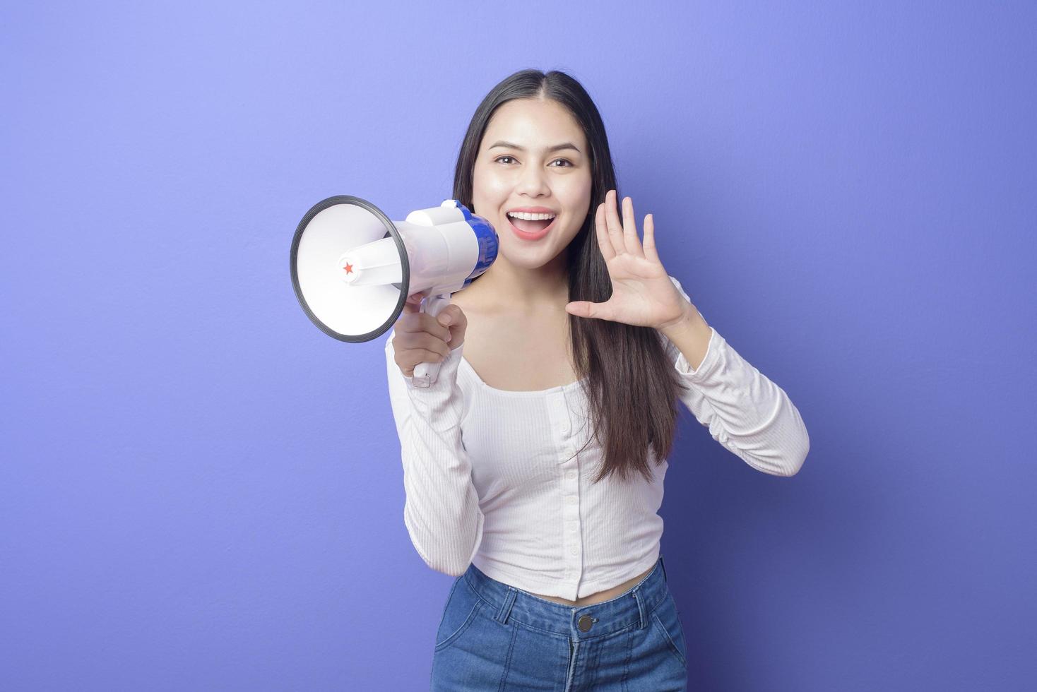 Porträt der jungen schönen lächelnden Frau benutzt Megaphon, um über isoliertem lila Hintergrundstudio zu verkünden foto