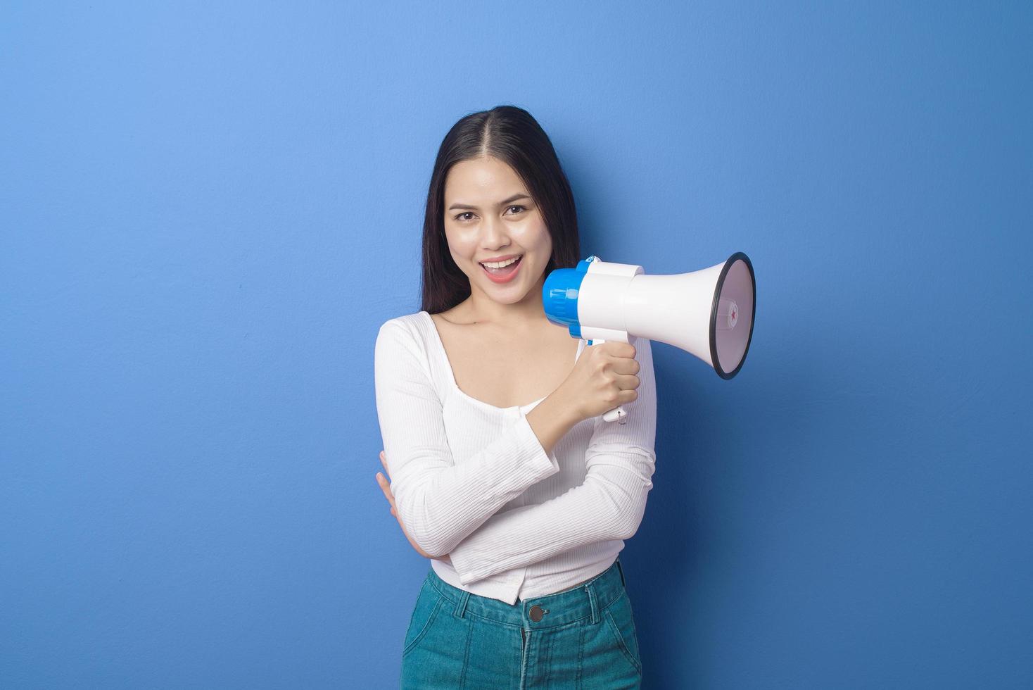 Porträt der jungen schönen lächelnden Frau benutzt Megaphon, um über isoliertem blauem Hintergrundstudio zu verkünden foto