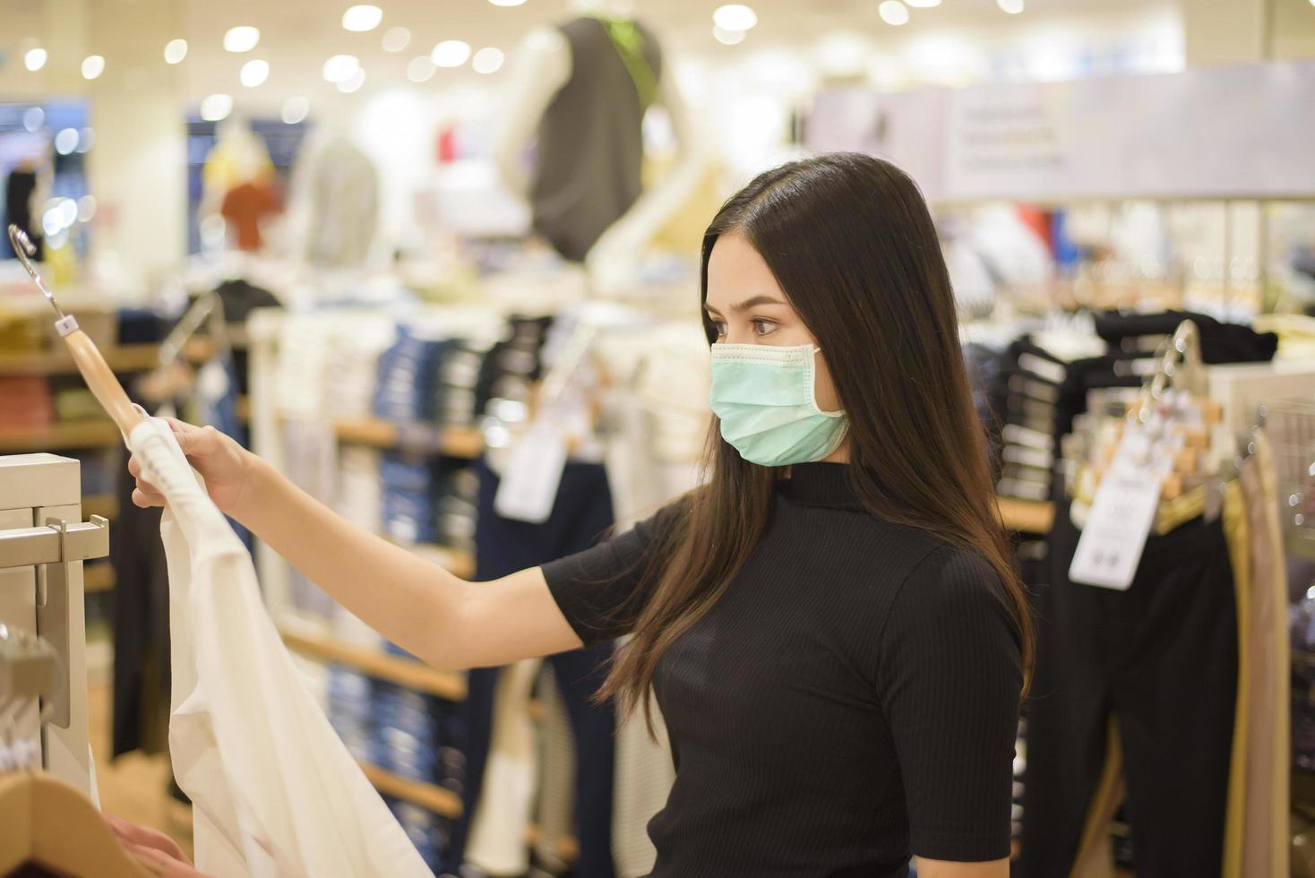 Frau mit Gesichtsmaske kauft Kleidung im Einkaufszentrum foto