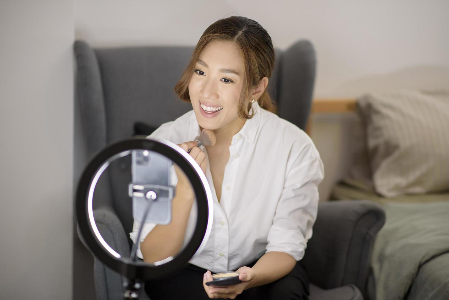 Eine schöne asiatische Make-up-Bloggerin streamt live, wie man in ihrem Haus-, Schönheits- und Technologiekonzept Schönheits-Gesichts-Make-up macht foto