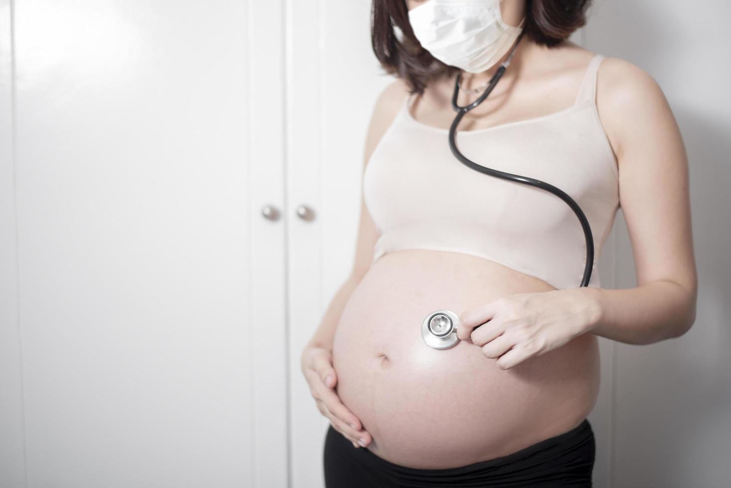 schöne asiatische schwangere frau trägt schutzmaske in ihrem haus, coronavirus-schutzkonzept foto