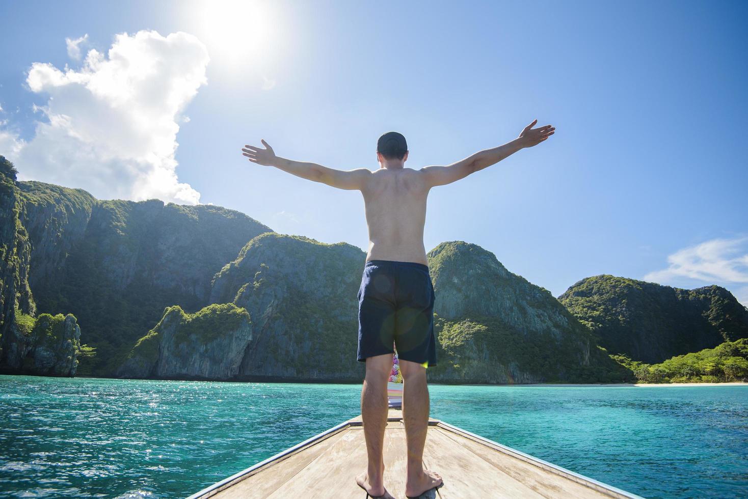 Blick auf den Mann im Badeanzug, der auf einem traditionellen thailändischen Longtail-Boot über schöne Berge und das Meer, die Phi-Phi-Inseln, thailand, genießt foto