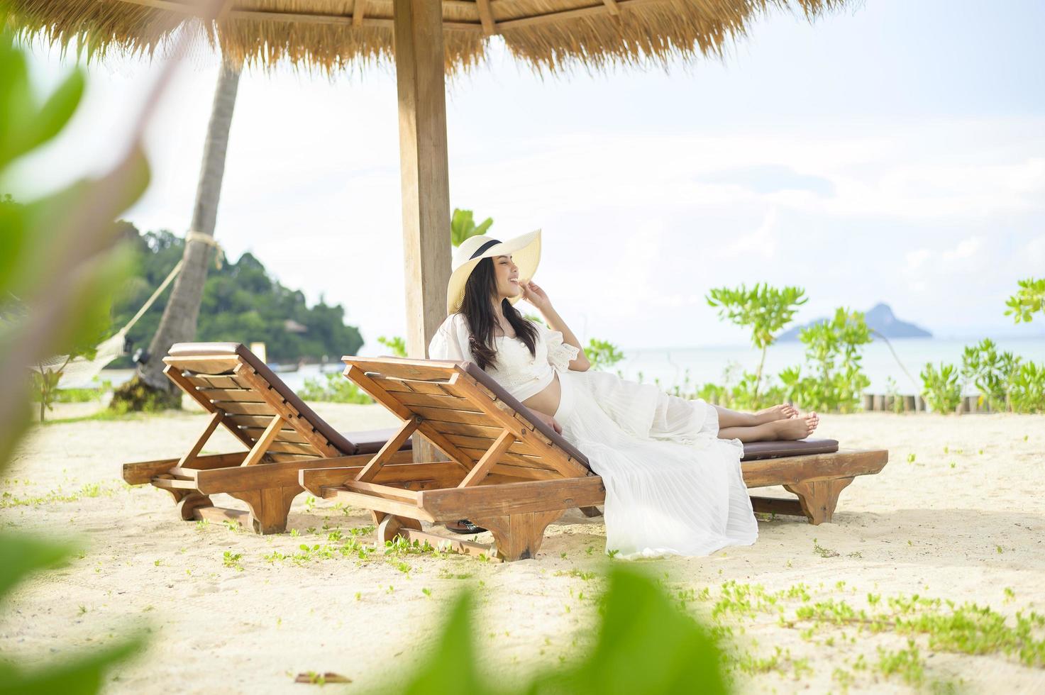 Eine junge Frau, die sich entspannt und auf dem Liegestuhl sitzt und im Urlaub auf den schönen Strand blickt foto