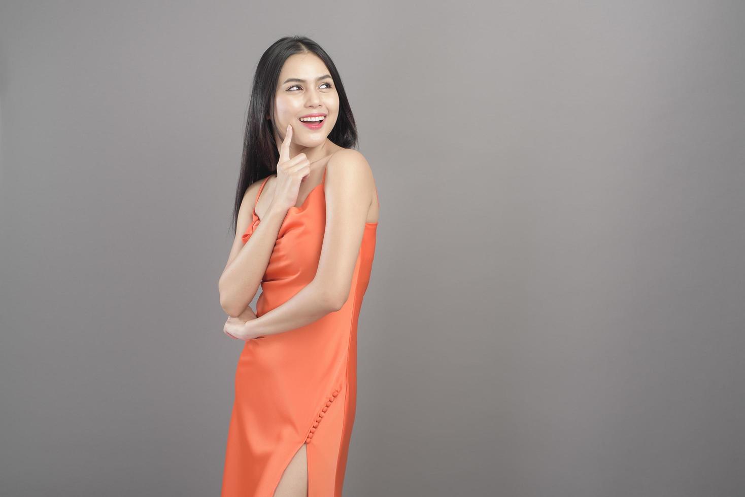 Modeporträt einer schönen Frau, die ein orangefarbenes Kleid trägt, isoliert über grauem Hintergrundstudio foto