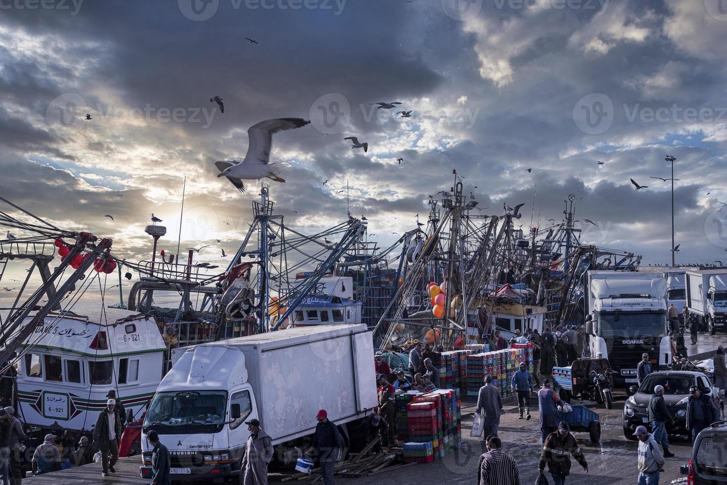 Leute laufen neben Lastwagen und Fischerbooten am Jachthafen auf dem Markt herum foto
