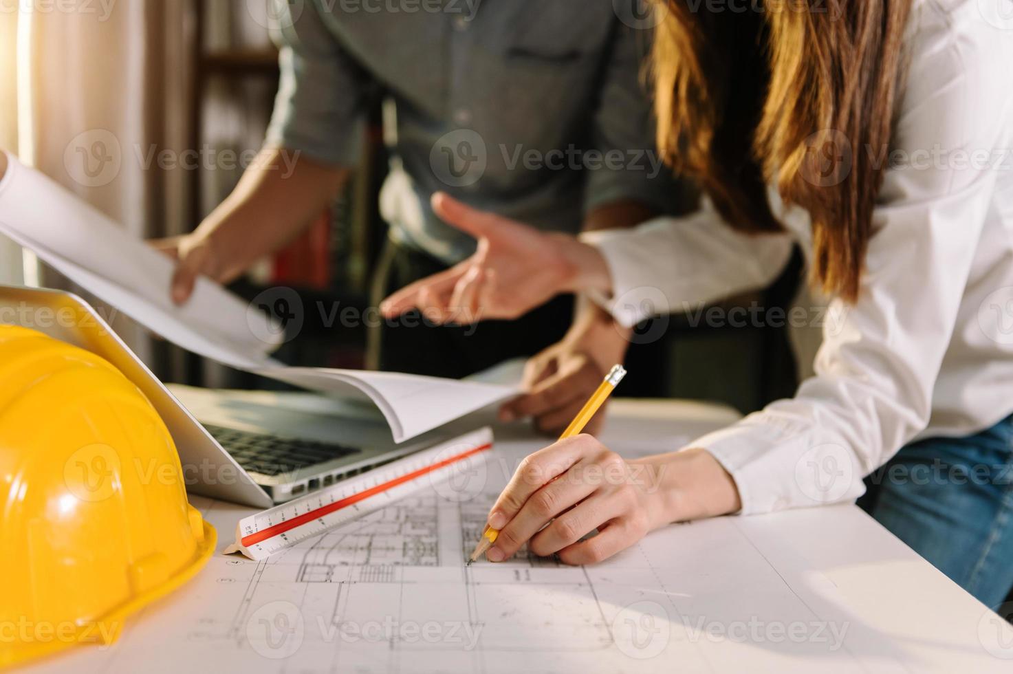 Zwei Kollegen diskutieren Datenarbeit und Tablet, Laptop mit eingeschaltetem Architekturprojekt auf der Baustelle am Schreibtisch foto