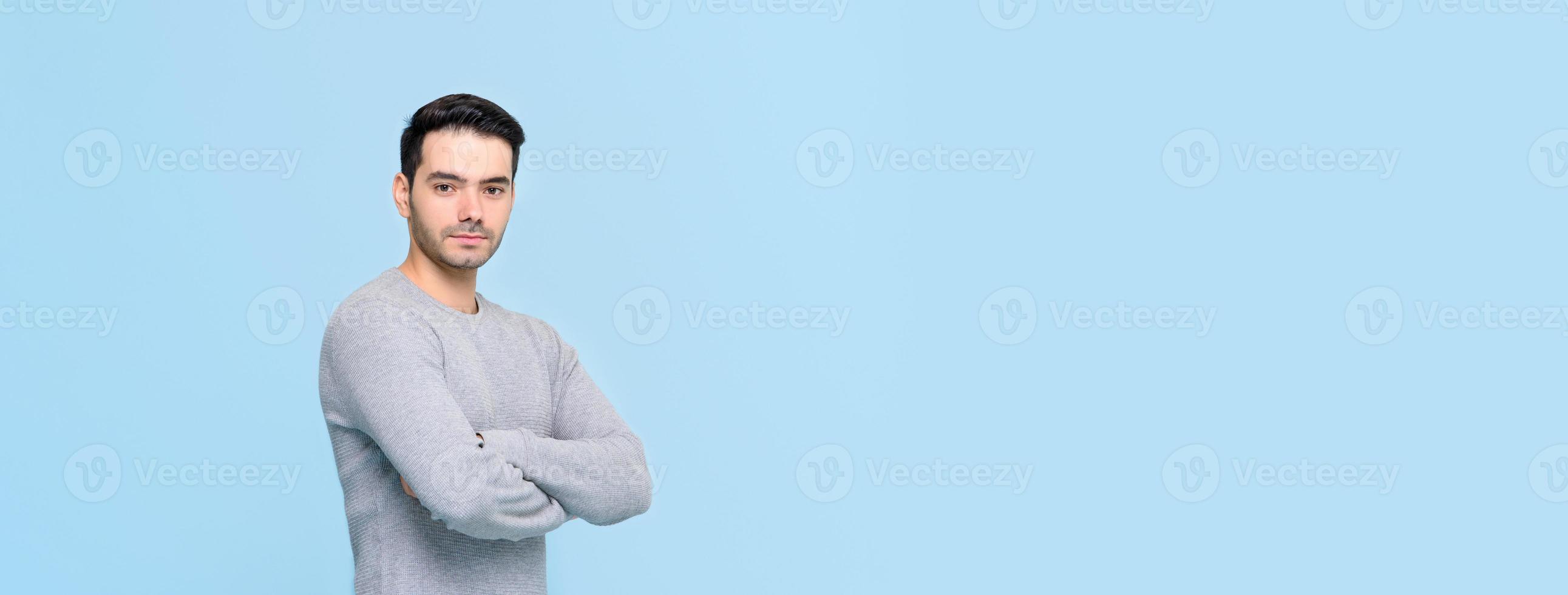 Selbstbewusster, gutaussehender Mann in lässigem grauem T-Shirt, der die Geste mit gekreuzten Armen einzeln auf hellblauem Bannerhintergrund mit Kopienraum macht foto