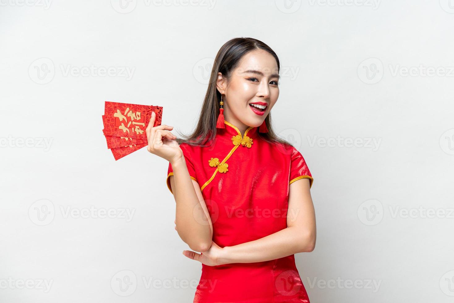 Lächelnde asiatische Frau in orientalischem Cheongsam-Kostüm mit roten Umschlägen oder Ang Pao einzeln auf hellgrauem Studiohintergrund für chinesische Neujahrskonzepte, Text bedeutet viel Glück, großen Gewinn foto