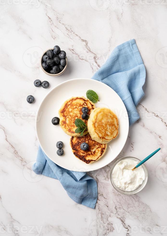 Hüttenkäsepfannkuchen serviert mit Quark und Blaubeeren, Draufsicht flach auf Marmorhintergrund foto