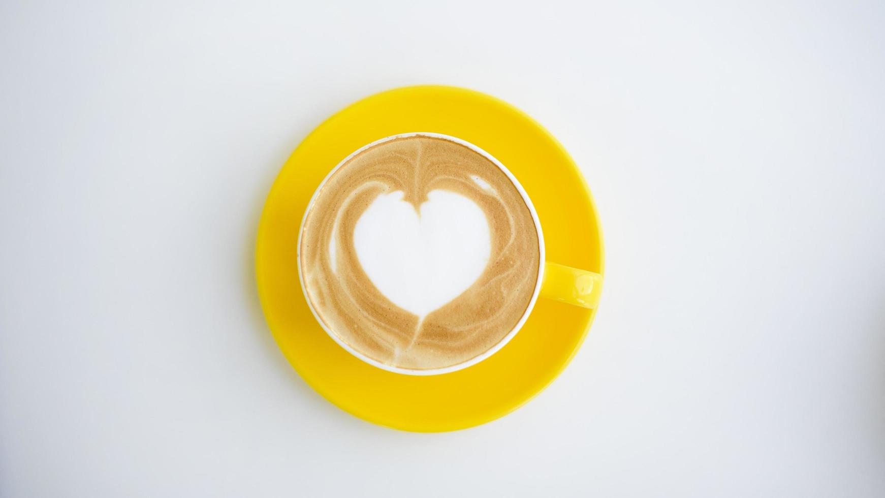 Heiße Latte Art in gelber Tasse auf dem Schreibtisch foto