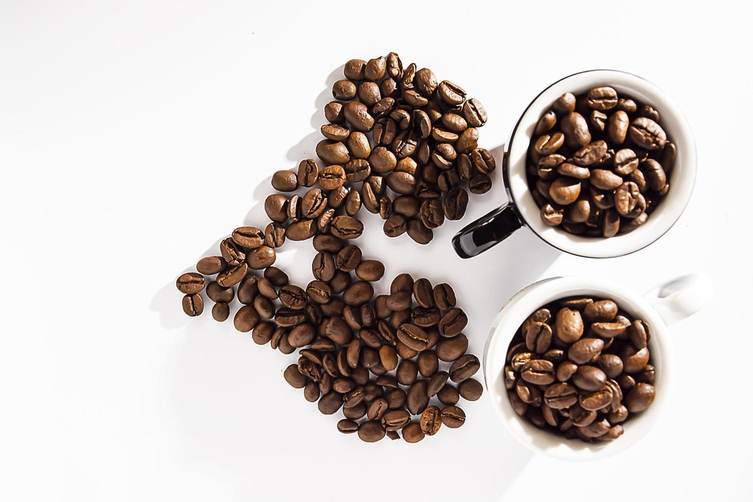 Schwarze und weiße Kaffeetassen mit Kaffeebohnen, die in Form eines Herzens auf weißem Hintergrund angeordnet sind. Lebensstil. flach. isolieren. Exemplar. foto