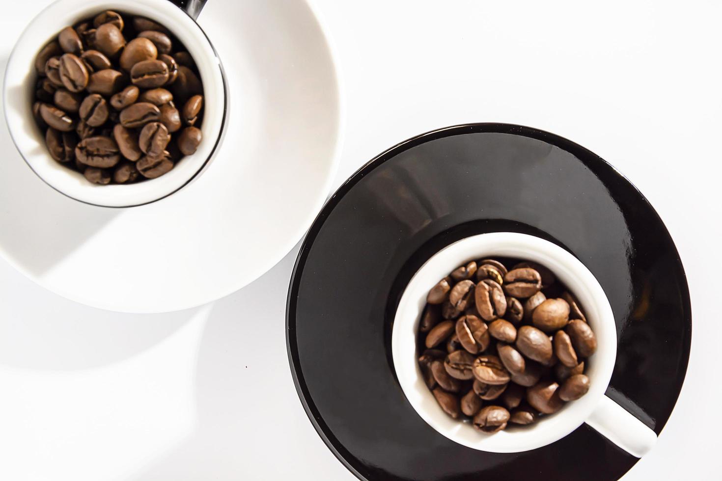 schwarz-weiße Espressotassen mit Kaffeebohnen auf Untertassen auf weißem Hintergrund. Lebensstil. Ihren eigenen Raum. flach. foto