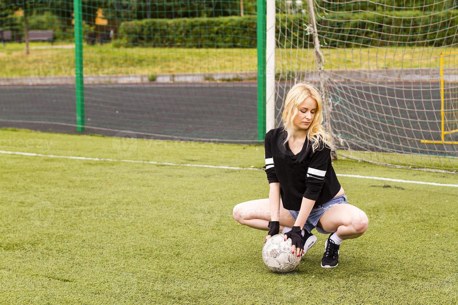 Das Mädchen sitzt mit dem Ball auf dem Fußballplatz. foto