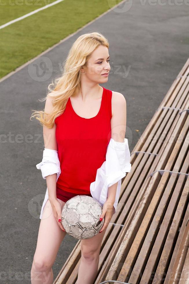 Fußballspielerin steht mit dem Ball auf der Bank in Rot. foto