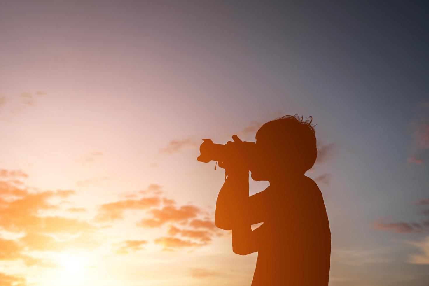 Silhouette eines jungen Mannes mit Kamera, strecken Sie die Arme während des Sonnenuntergangs aus. foto