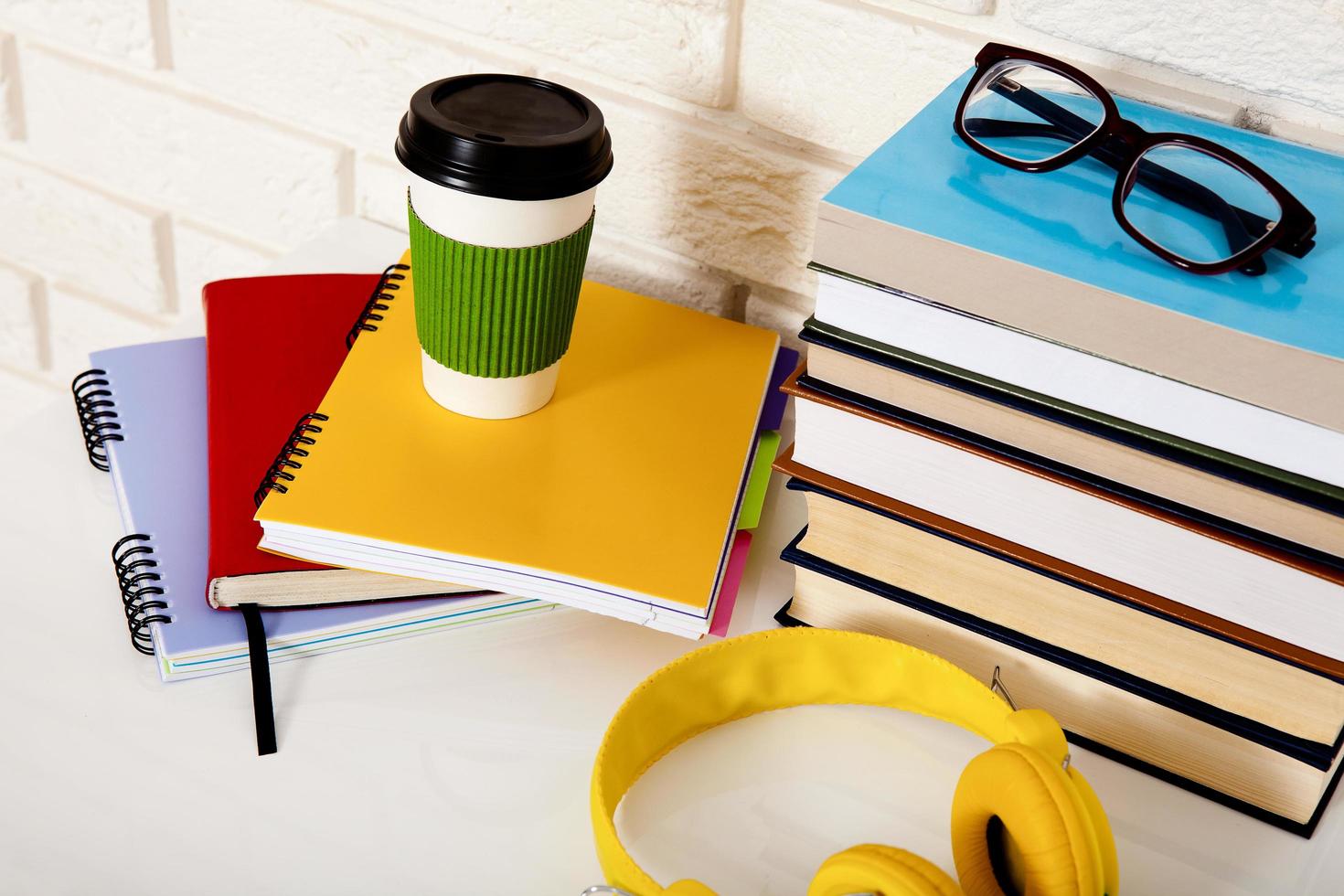 arbeitsplatz- und bildungszubehör auf dem tisch. Tasse Kaffee, Bücher, Gläser, Notizbücher, Kopfhörer. Bildung aufhalten foto