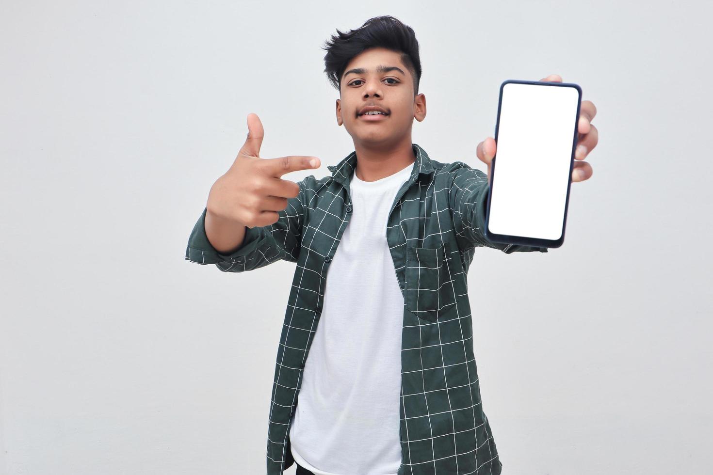 junger indischer Collagenjunge, der Smartphone-Bildschirm auf weißem Hintergrund zeigt. foto