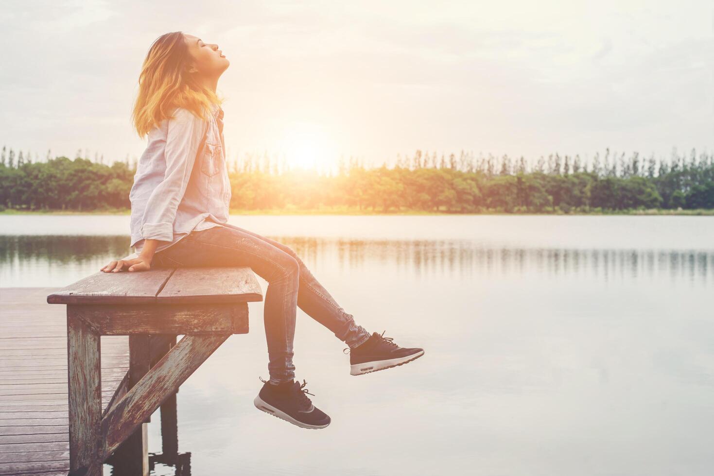 junge schöne hipster-frau, die auf dem see sitzt und sich an der frischen luft entspannt. foto