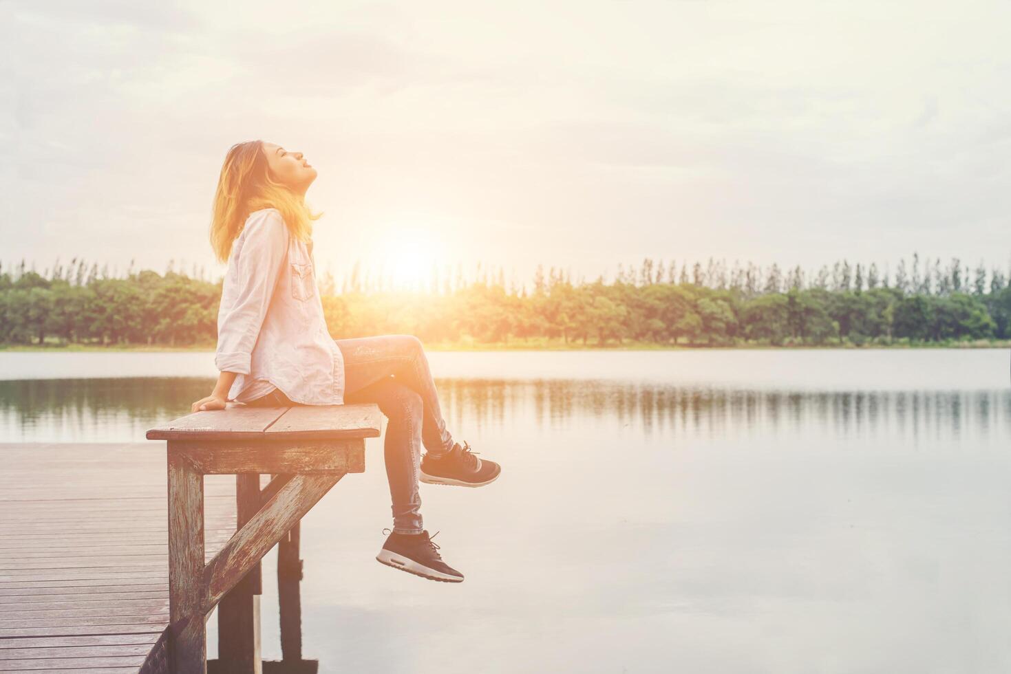 junge schöne hipster-frau, die auf dem see sitzt und sich an der frischen luft entspannt. foto