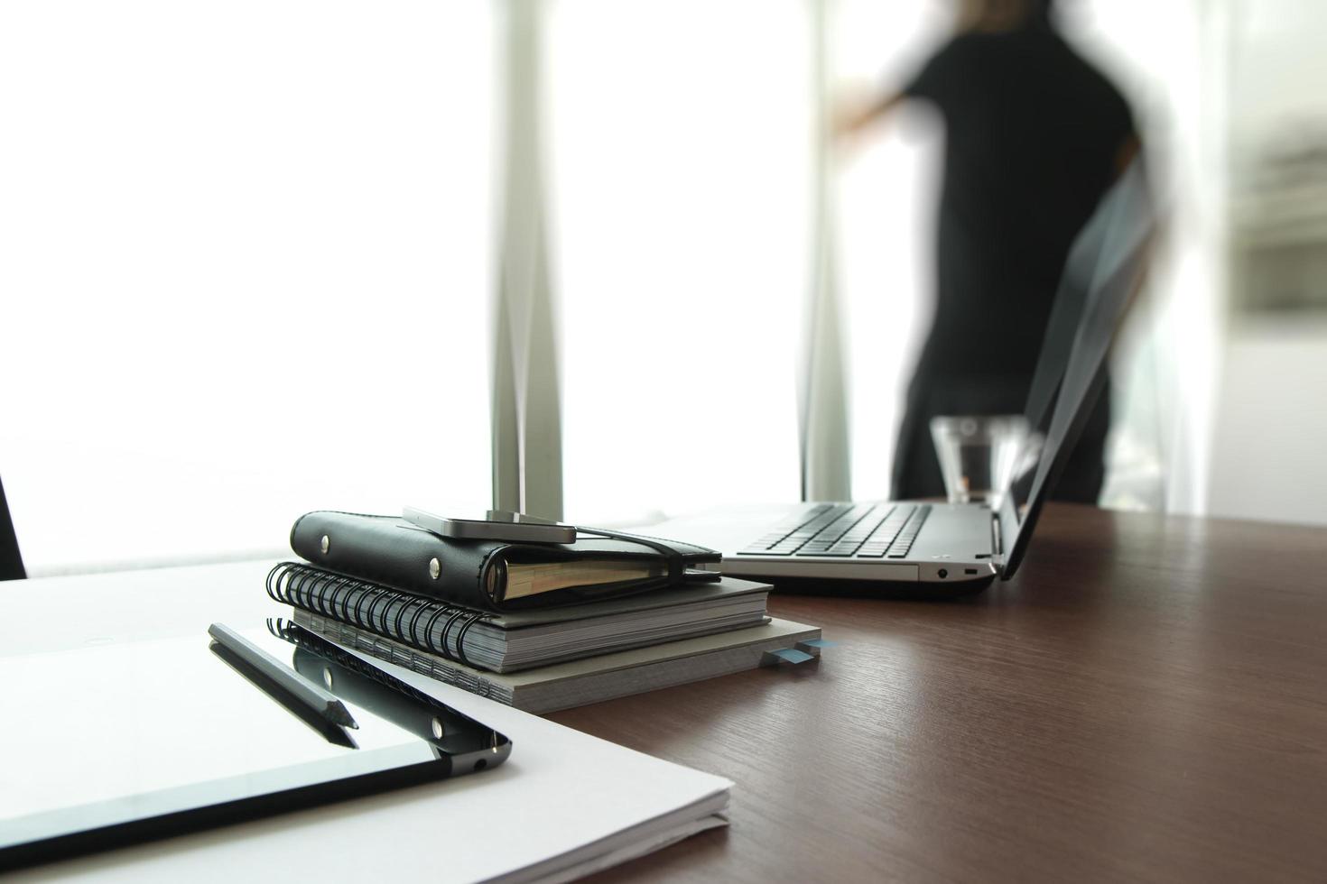 Geschäftsdokumente auf Bürotisch mit Smartphone und digitalem Tablet und Mann, die im Hintergrund arbeiten foto