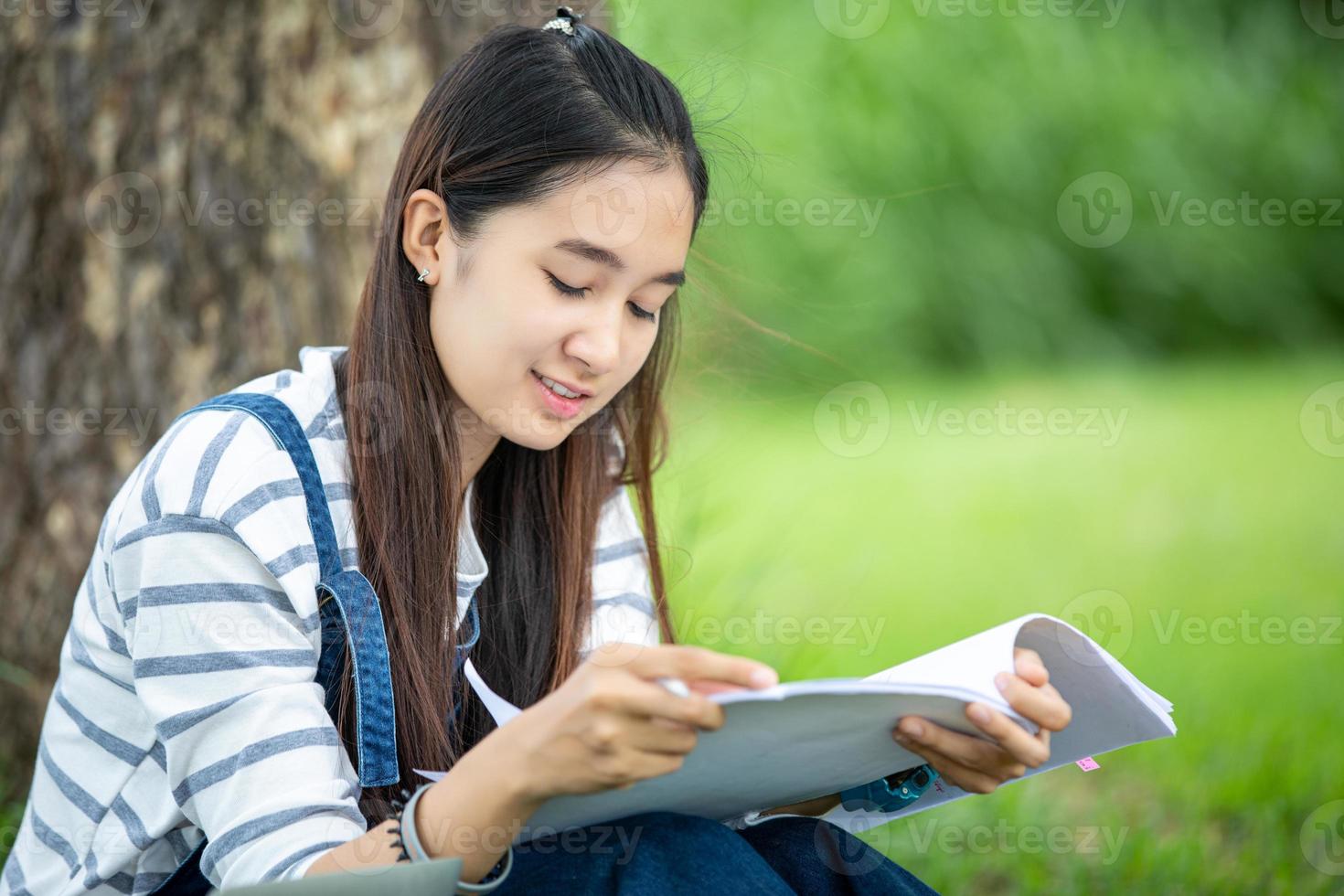 schöne asiatische studentin, die bücher hält und in die kamera lächelt und im sommer ein lern- und bildungskonzept im park zur entspannungszeit hat foto