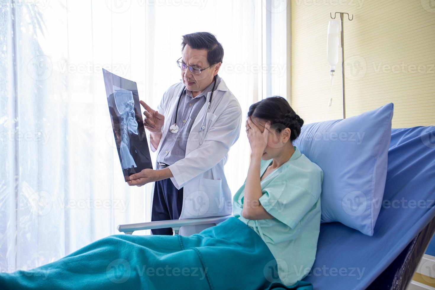 Der Arzt erklärt einer Patientin, die in einem Krankenhaus im Bett liegt, über die Röntgenergebnisse des Gehirns foto