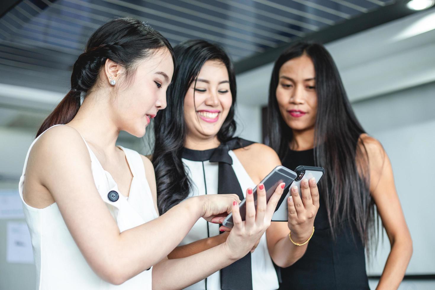 Asiatische Geschäftsfrauen mit Partner diskutieren über die Details der Arbeit am Smartphone und Geschäftsfrauen lächelnd foto