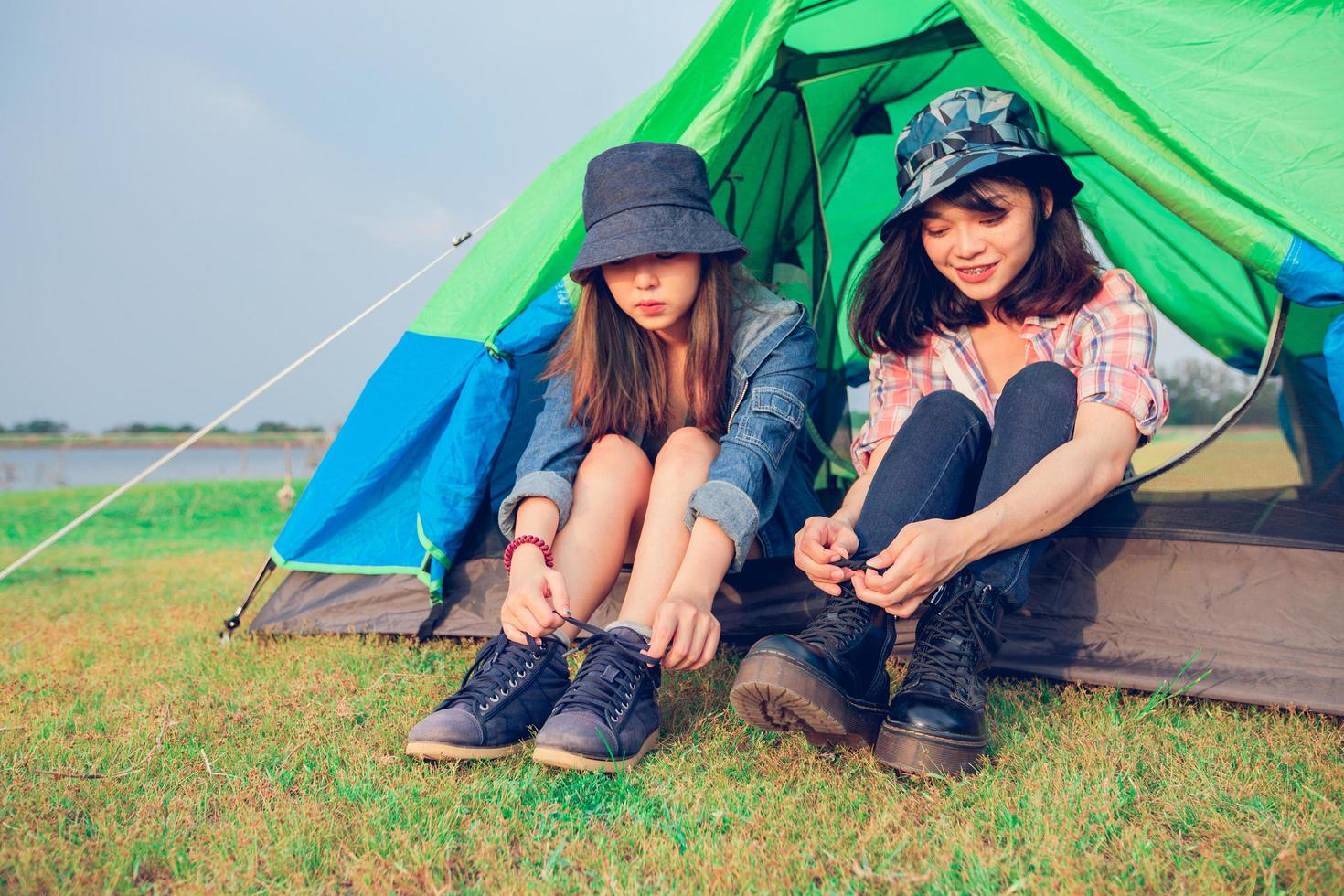 Eine Gruppe asiatischer Touristenfreunde bindet im Sommer glücklich einen Schuh in der Nähe des Zeltes, während sie campen foto