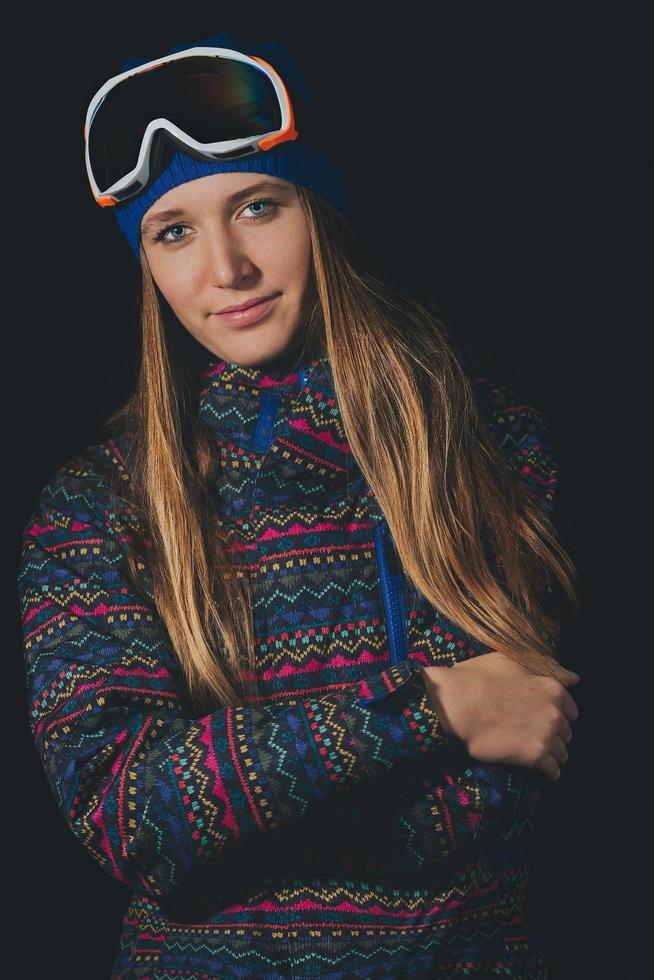 schönes blondes Mädchen mit langen Haaren in Snowboardkleidung mit schwarzem Hintergrund foto