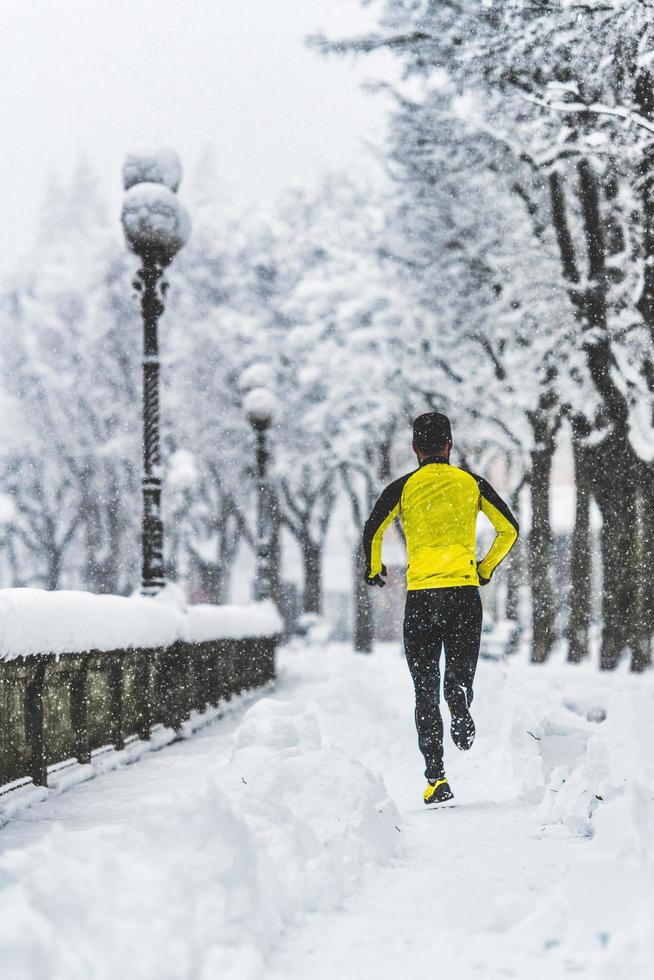 Junger Mann läuft im Winter auf verschneitem Bürgersteig foto