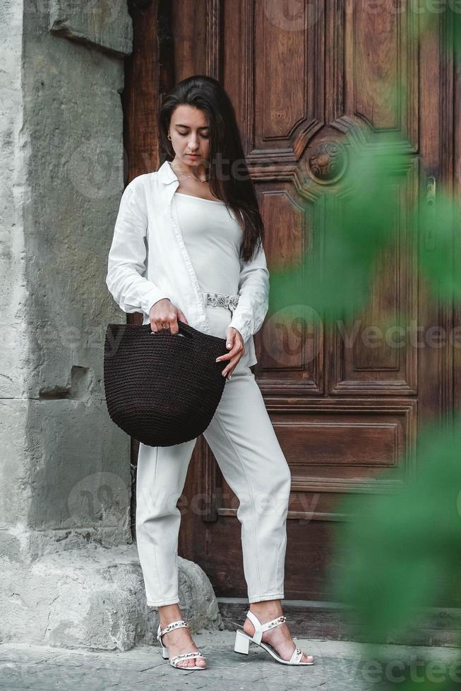 Frau in weißer Kleidung, mit gestrickter Tasche auf dem Hintergrund alter Holztüren. kopieren, leerer platz für text foto