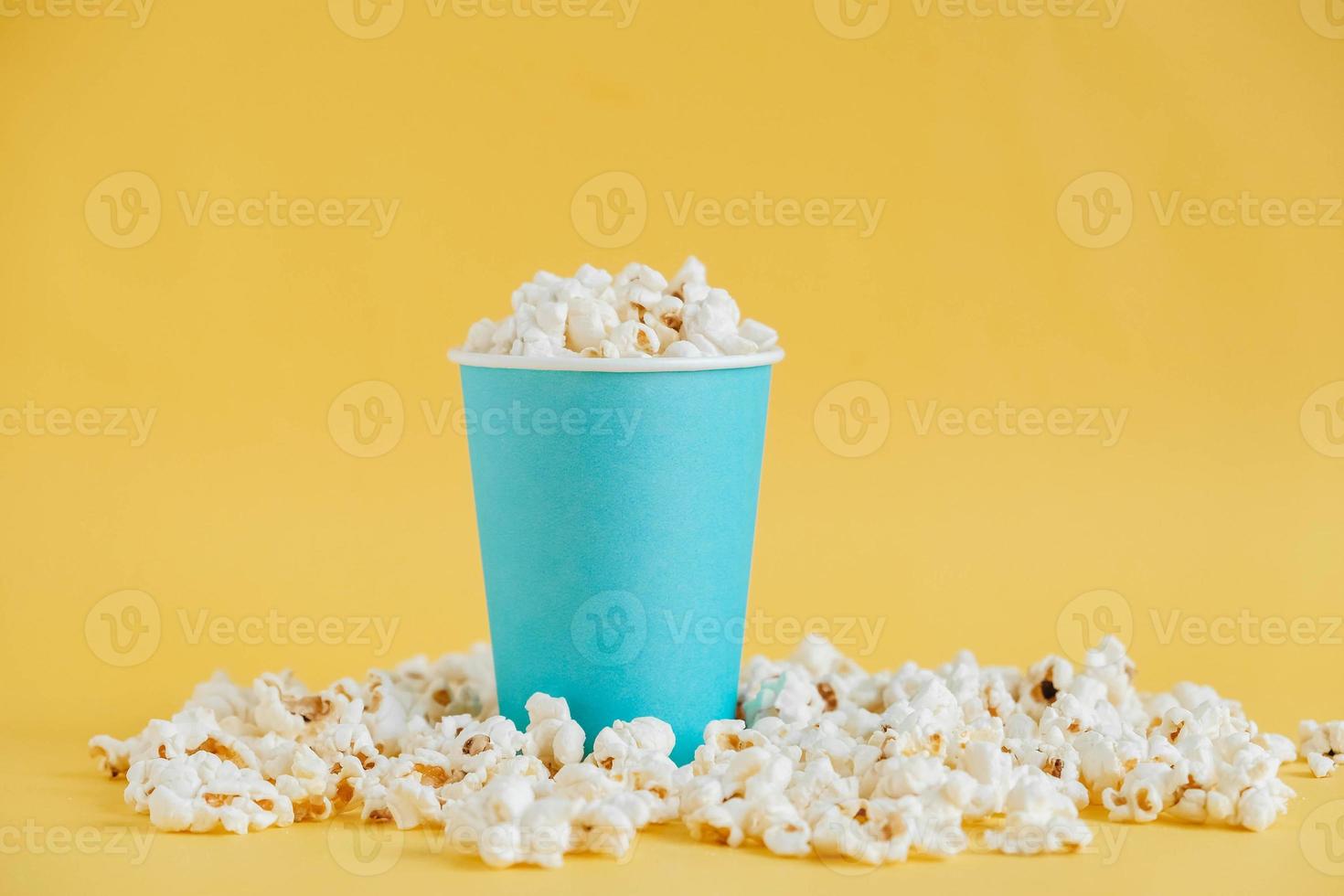 Popcorn in einem blauen Pappbecher auf gelbem Hintergrund. minimalistisches Konzept. kopieren, leerer platz für text foto