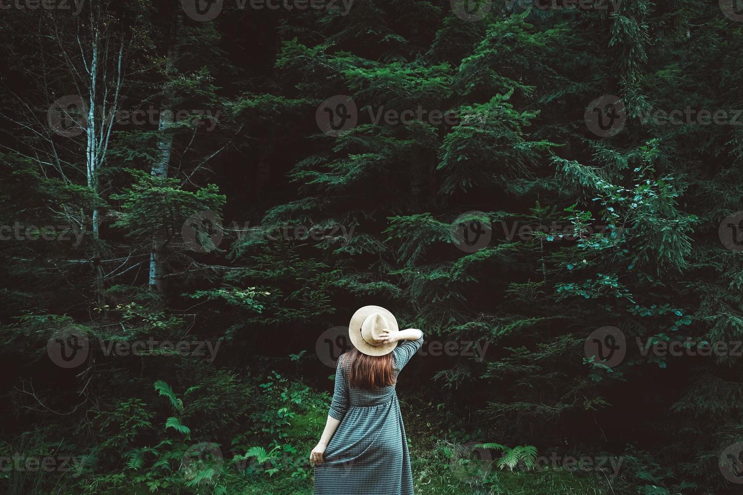 Frau mit Strohhut und Kleid steht auf einem Hintergrund aus grünem Wald und Bäumen foto