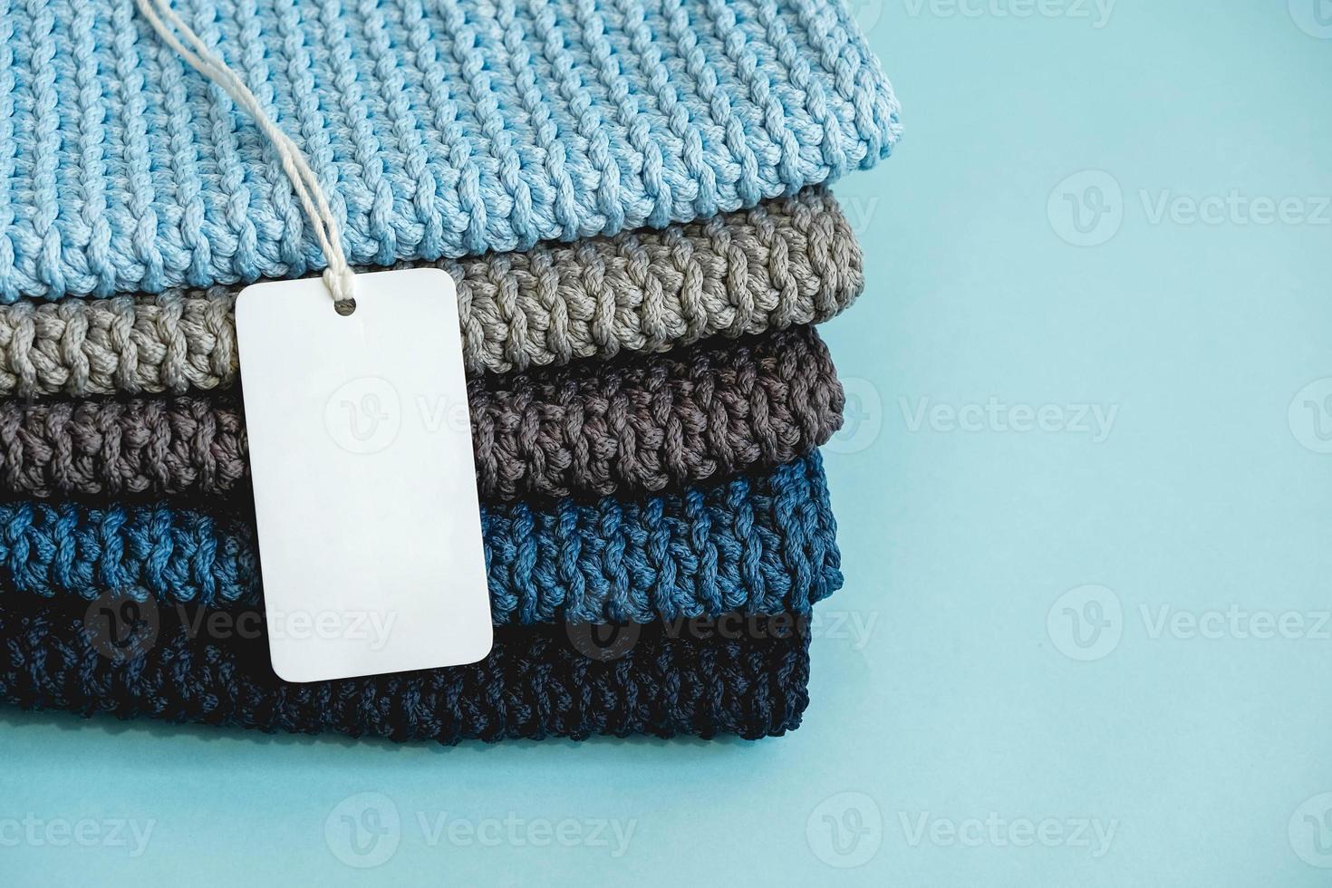 Stapel von Strickmaterial aus dunkelblauen, hellblauen, grauen Fäden mit leerem Preisschild auf blauem Hintergrund. kopieren, leerer platz für text foto