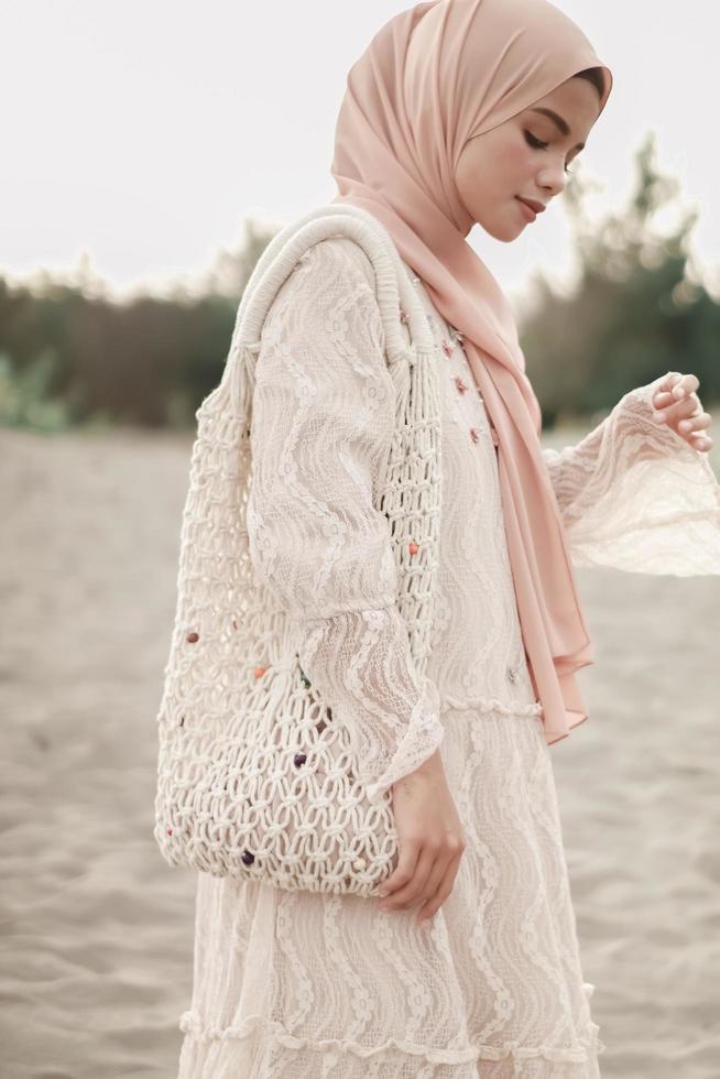 Schönes islamisches weibliches Modell in Hijab-Mode, ein modernes Hochzeitskleid für muslimische Frauen geht am Sand und am Meer entlang. ein asiatisches mädchenmodell, das hijab verwendet, das spaß am strand hat. Foto vor der Hochzeit