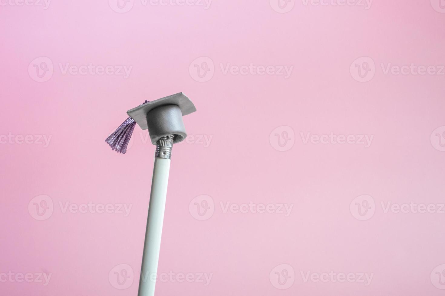 weißer Bleistift mit Graduierungshut auf einer rosa Hintergrundnahaufnahme mit Kopienraum. Bildungskonzept foto