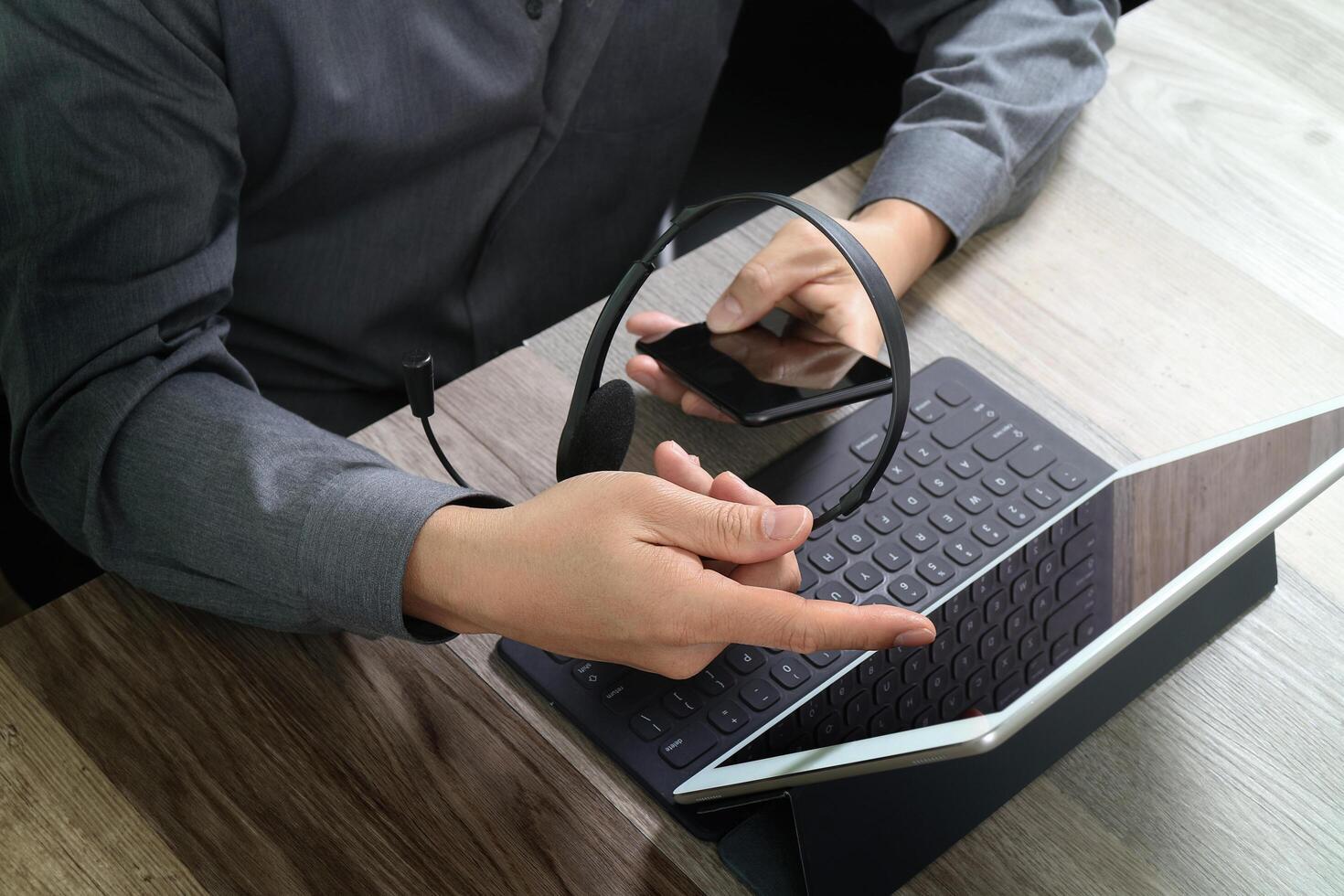 Draufsicht der Hand des Mannes mit VoIP-Headset mit digitaler Tablet-Computer-Docking-Tastatur, Smartphone, Konzeptkommunikation, IT-Support, Callcenter und Kundendienst-Helpdesk auf Holztisch foto