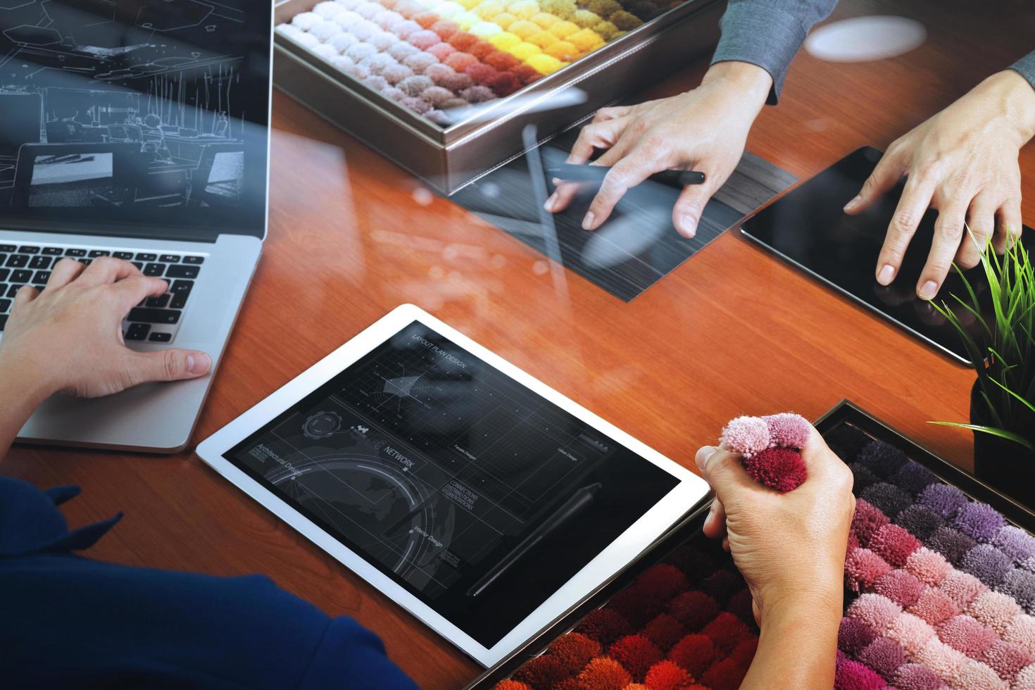 Draufsicht auf zwei Innenarchitekten, die Daten mit einem neuen modernen Computer-Laptop und einem digitalen Pro-Tablet mit Mustermaterial auf einem Holzschreibtisch als Konzept diskutieren foto