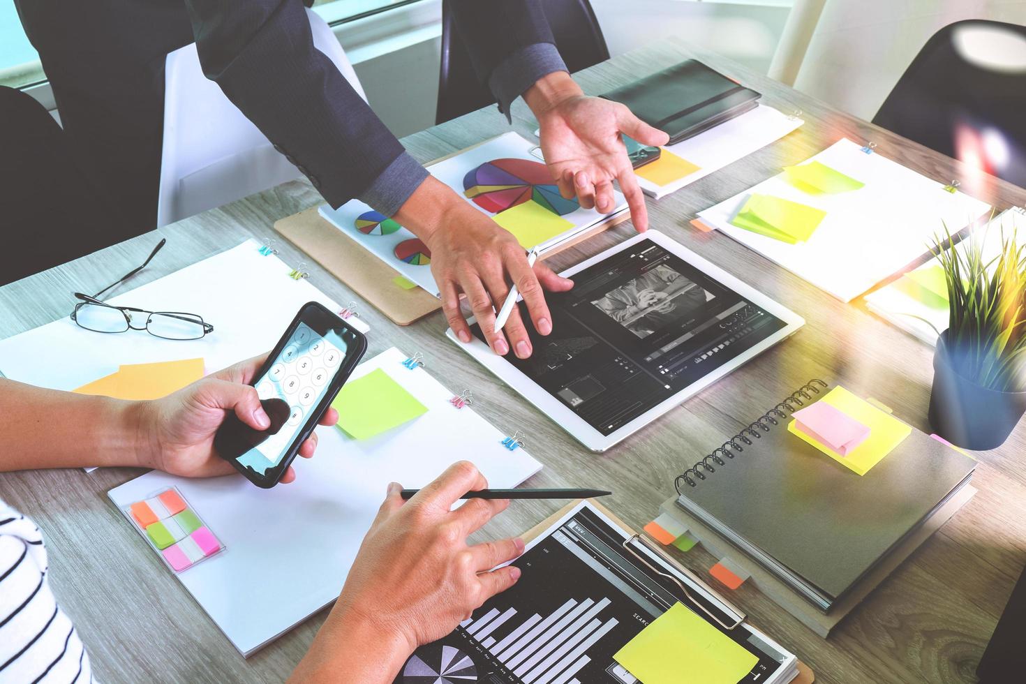 Geschäftsdokumente auf Bürotisch mit Smartphone und Laptop und Grafikgeschäft mit sozialem Netzwerkdiagramm und zwei Kollegen, die Daten im Hintergrund diskutieren foto