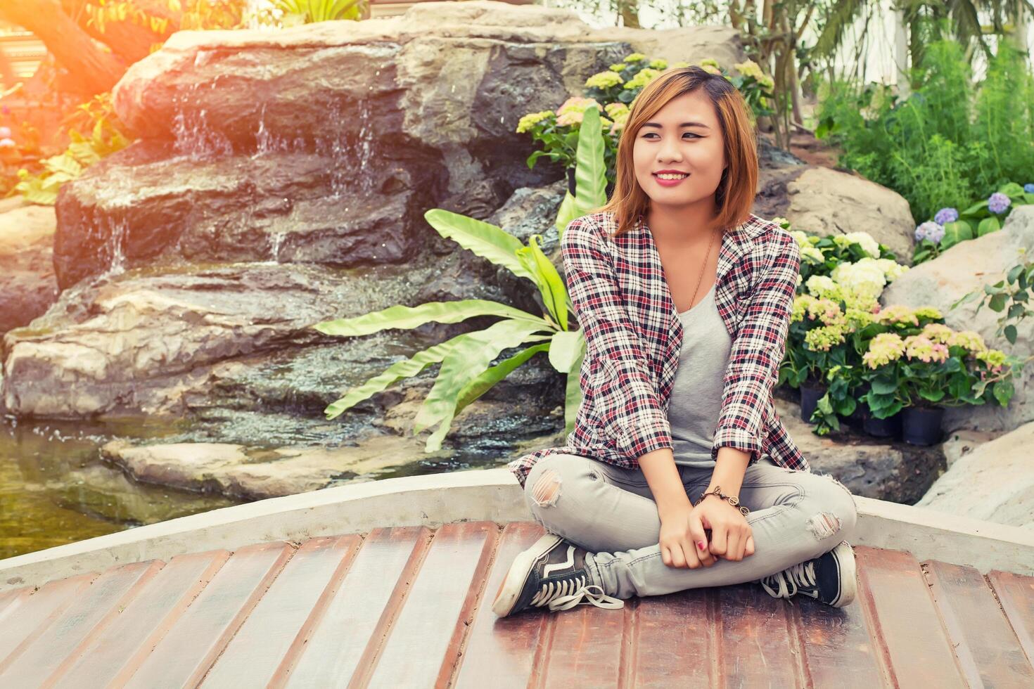 Junge schöne Hipster-Frau, die im Flora-Garten in der Nähe des Wasserfall-Smileys sitzt, so glücklich. foto
