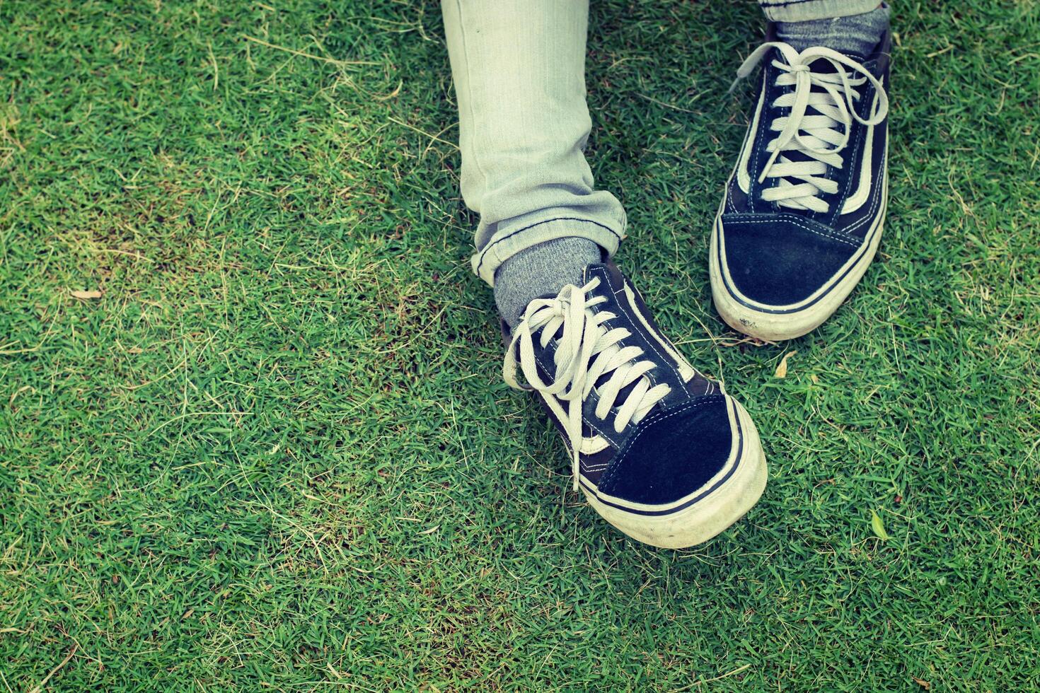 Frauenbeine in Jeans mit Turnschuhen, die auf dem Gras sitzen. foto