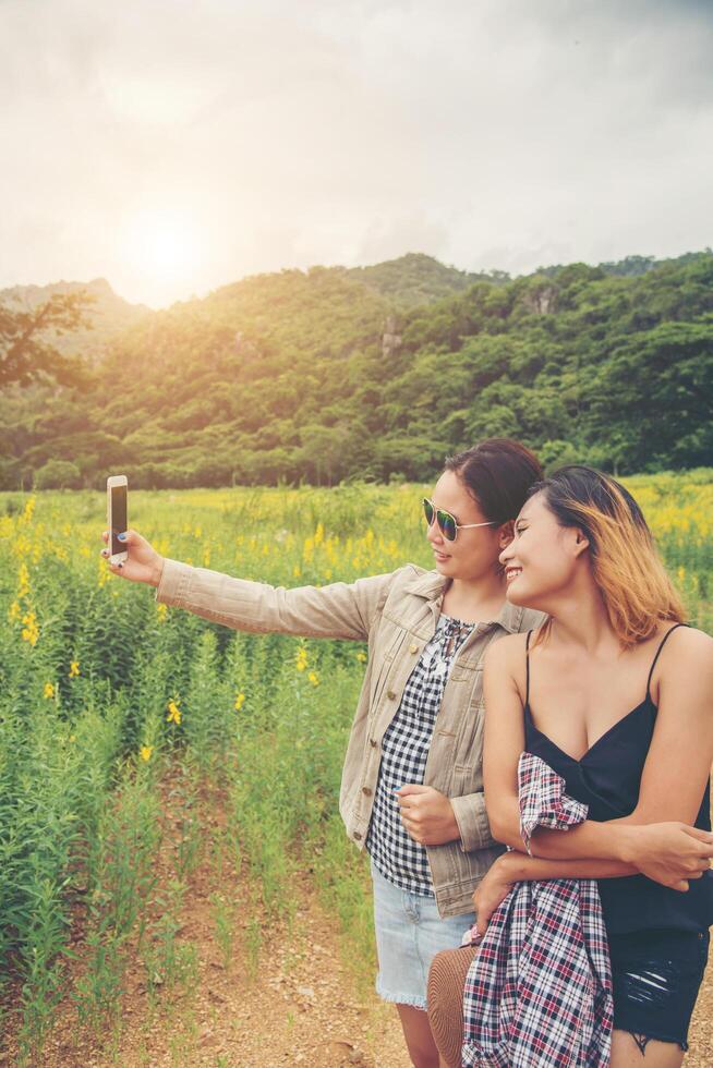 Freunde machen Selfies. zwei schöne junge frau, die selfie im feld mit gelben blumen nimmt. foto