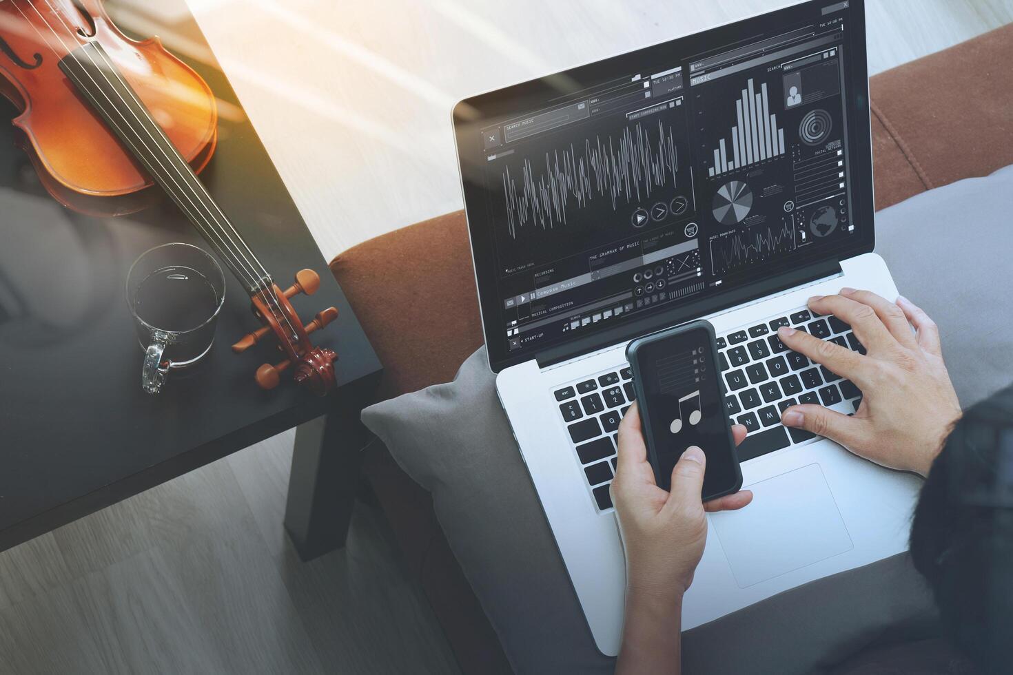 Hipster handkomponiert Musik mit Smartphone und Laptop und sitzt auf dem Sofa im Heimstudio foto