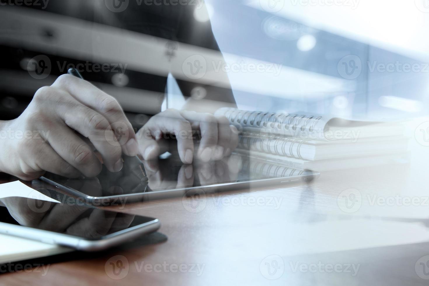 Designerhand, die mit digitalem Tablett und Laptop und Notizbuchstapel und Augenglas auf Holzschreibtisch im Büro arbeitet foto