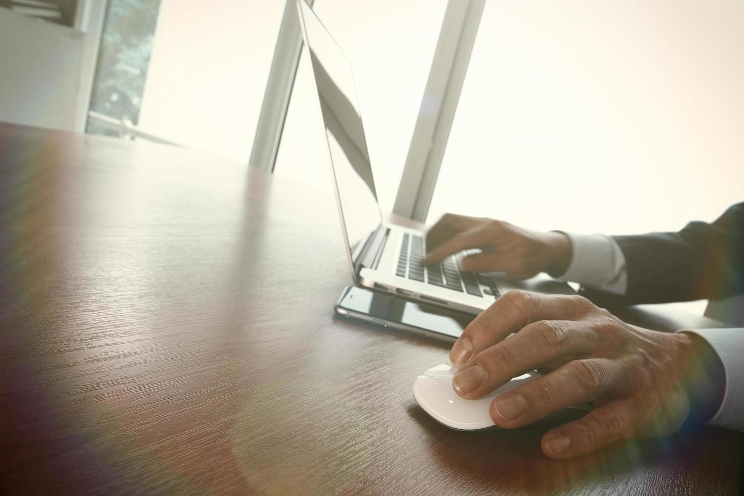 Geschäftsmannhand, die an Laptop-Computer auf hölzernem Schreibtisch arbeitet foto