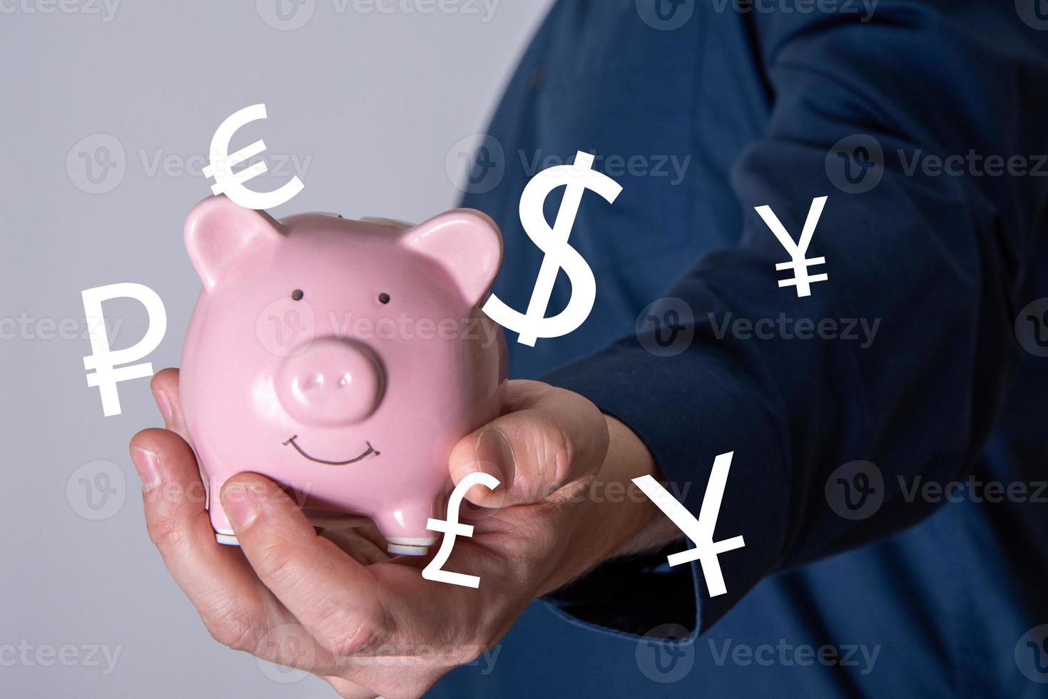 Ein nicht erkennbarer Geschäftsmann, der ein funkelndes rosa Sparschwein mit Währungssymbolen aus der ganzen Welt hält. foto