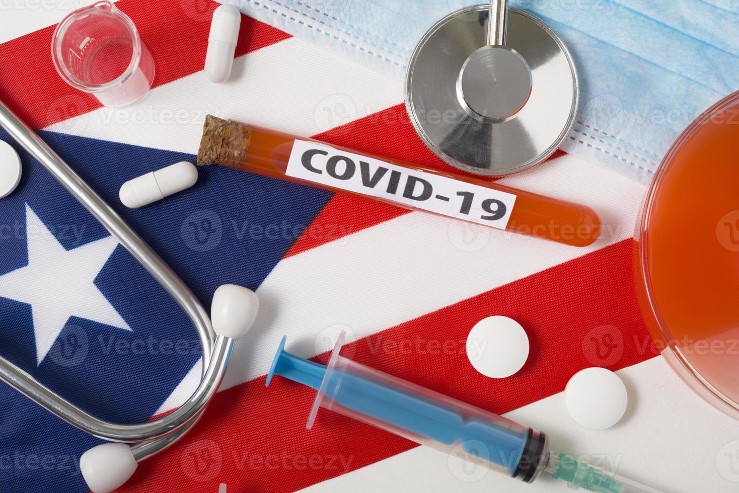 Coronavirus, das Konzept Covid-19. Draufsicht Atemschutzmaske, Stethoskop, Spritze, Tabletten auf der Flagge des Würfels. foto