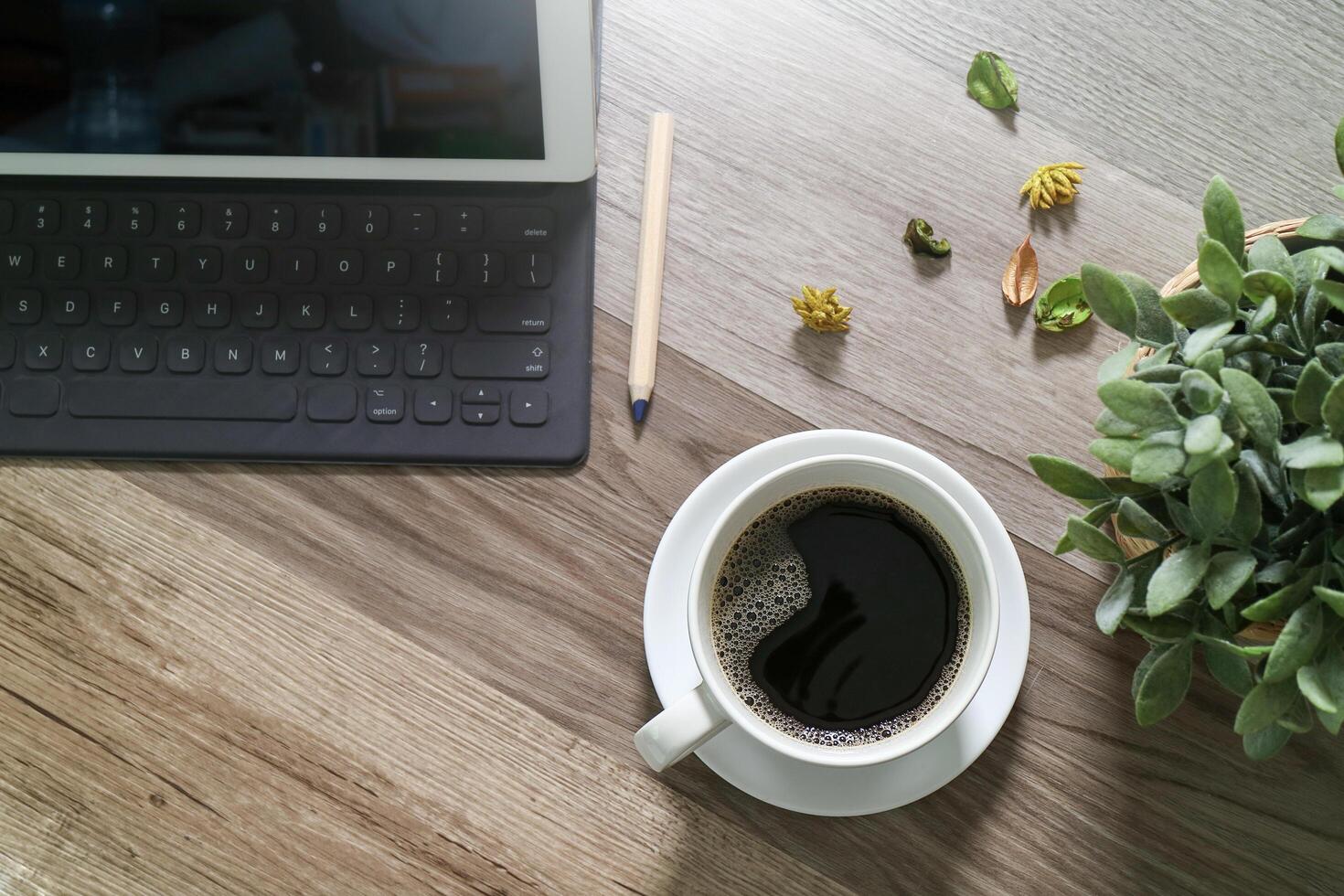 kaffeetasse und digitaler tisch docken intelligente tastatur, vasenblumenkräuter, stift auf holztisch, filtereffekt an foto