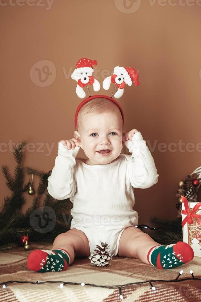 schöner kleiner Junge, der Weihnachten feiert. lustiges kind, das in einem weihnachtsanzug nahe weihnachtsbaum im zimmer trägt foto